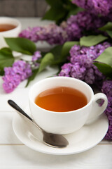 A cup of green tea against the background of a spring bouquet of lilacs on a textured gray background.Romantic composition with books and candles. Spring tea drink. Place to copy.
