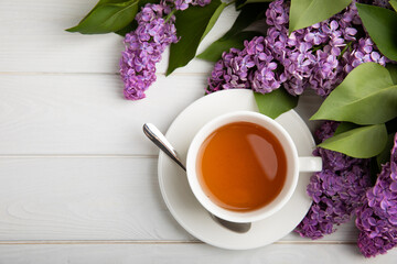 A cup of green tea against the background of a spring bouquet of lilacs on a textured gray background.Romantic composition with books and candles. Spring tea drink. Place to copy.