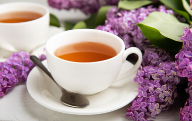 A cup of green tea against the background of a spring bouquet of lilacs on a textured gray background.Romantic composition with books and candles. Spring tea drink. Place to copy.