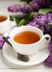 A cup of green tea against the background of a spring bouquet of lilacs on a textured gray background.Romantic composition with books and candles. Spring tea drink. Place to copy.