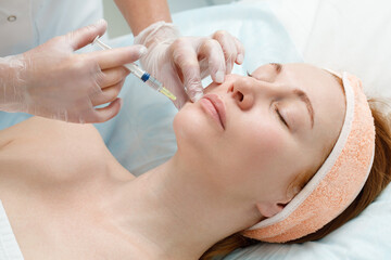 Cosmetologist performs the chin lift procedure by injecting beauty injections. Doctor injecting hyaluronic acid into the ching of a woman as a facial rejuvenation treatment.