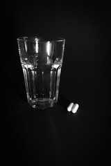 next to a glass of water are 2 white pills