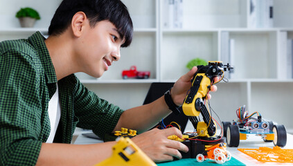 Asian teenager doing robot arm homework project in house, technology of robotics programing and...
