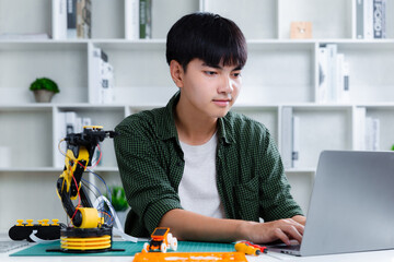 Asian teenager constructing robot arm homework project with laptop in house. technology of robotics programing and STEM education concept.