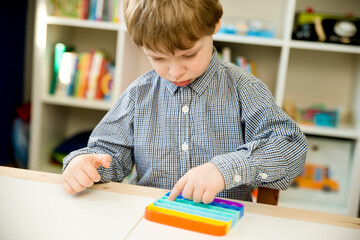 Child plays with sensory fidget toy Pop-it. Instrument for fine motoric skils, tool to start...