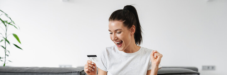 Excited woman making winner gesture while using credit card and laptop