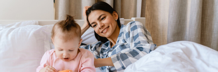 Young mother smiling and playing with her baby while lying in bad