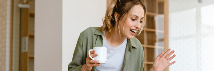 Young white woman gesturing while drinking coffee and using laptop