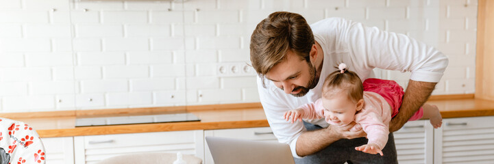 White father smiling and playing with his daughter while using laptop