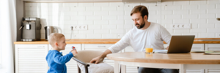 White father playing with his son and using laptop in kitchen