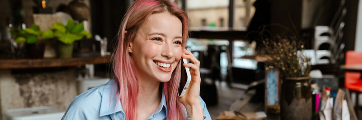 Young smiling woman talking on mobile phone while drinking coffee