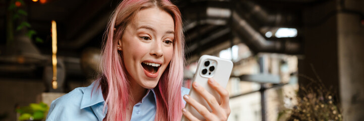 Young excited woman using mobile phone while drinking coffee in cafe