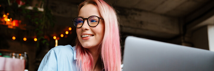 Young smiling woman working with laptop while sitting in cafe