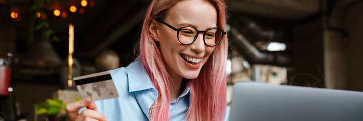 Young smiling woman using laptop and credit card while sitting in cafe