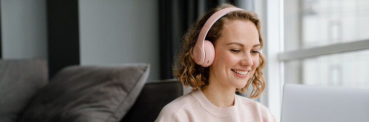 White woman in headphones using laptop while sitting on floor