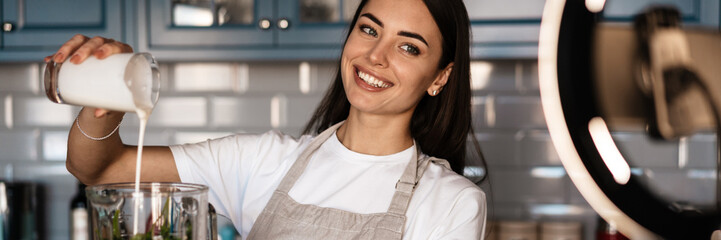 White smiling woman taking selfie on cellphone while preparing smoothie