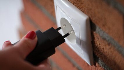 Closeup of woman holding hand and inserting plug into socket