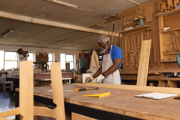 African american mature carpenter marking on plank at workbench in workshop