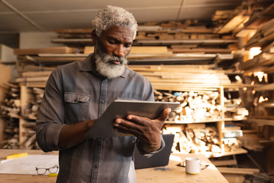 African american mature carpenter working on digital tablet in woodworking workshop