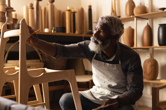 African american mature carpenter making chair in workshop - Powered by Adobe