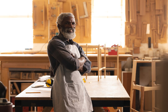 Portrait of smiling african american mature carpenter standing with arms crossed in workshop - Powered by Adobe