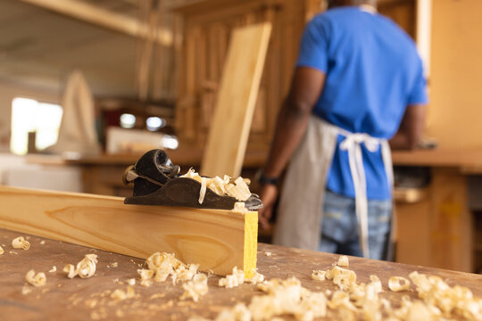 Close-up of planer on wood with african american mature carpenter in background
