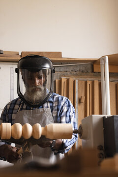 African american mature carpenter wearing safety face shield shaping and carving wood at workshop