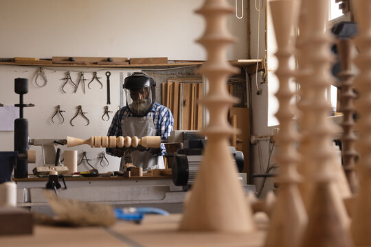 African american mature carpenter wearing safety face shield shaping and carving wood in workshop