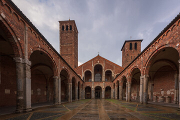 Saint Ambrogio church brick building with bell towers, courtyard, arches at overcast day, Milan,...
