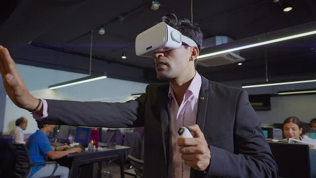 A moving shot of an Indian Asian corporate male or. man wearing VR or Virtual reality headsets or glasses and making hand gestures working on 3D Commercial designs or digital models in a modern office