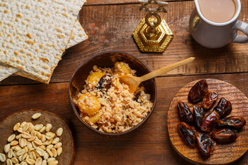 A plate of couscous with fruits and nuts on a wooden table next to matzah and a jug of fruit broth.