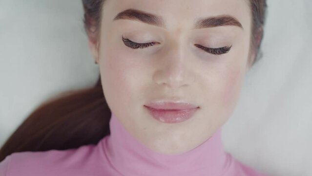 Lashmaker takes a patch from under the eyelashes of a beautiful young woman with gold tweezers