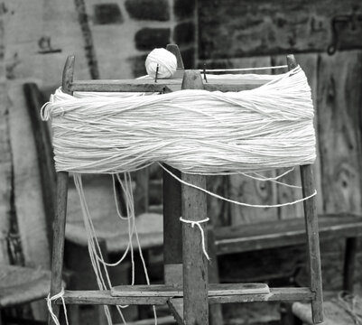 antique wooden spinning wheel with the skein of wool below and the ball of yarn above with an antique effect in black and white
