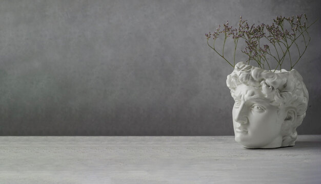 White copy plaster statue of the head of David on a gray concrete background. Minimal art poster. Ancient Greek sculpture. copy space. Banner. - Powered by Adobe