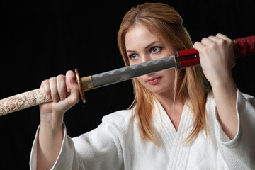 A young woman in a kimono holds a katana in front of her face and looks away