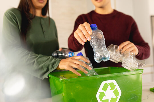 Midsection of asian young couple throwing plastic bottles in dustbin at home