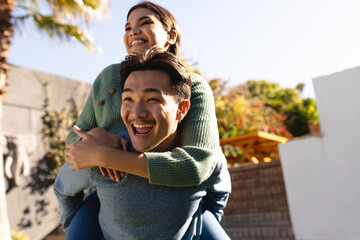 Cheerful young asian couple piggybacking in backyard on sunny day