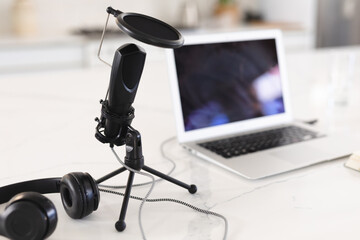 Close-up of microphone with headphones and laptop on white table at home, copy space