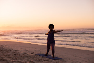 Silhouette african american mature woman practicing warrior 2 pose at beach against clear sky