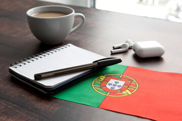portugal flag, headphones, notepad, pen and cup on wooden desk, the concept of learning foreign...
