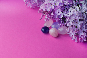 Beautiful pink lilac flowers and semi-precious stones, rose quartz and amethyst lie on a pink...