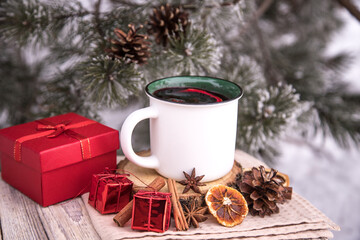 Warming mulled wine in a white cup with spices on the background of a snow-covered pine tree.