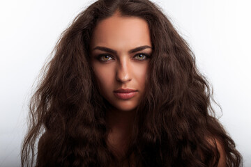 Sexy attractive young woman with long brown wavy curly fluffy hair looking at camera with confident...