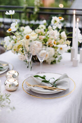 Banquet table is decorated with plates, cutlery, glasses and flower arrangements