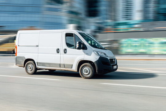 panel van Fiat Ducato 130 Multijet speeding on road. White delivery van in motion on the street, side view