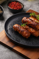 Traditional south european skinless sausages cevapcici made of ground meat and spices on black plate on dark wooden board, with thyme and watercress salad