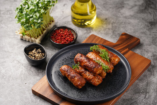 Traditional south european skinless sausages cevapcici made of ground meat and spices on black plate on dark wooden board, with thyme and watercress salad