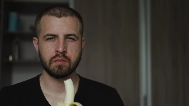 A man with a beard eats a banana.