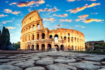 Naklejka na ściany i meble Sunset and Colosseum in Rome, Italy. Low angle view of the main facade of the Colosseum, and in the foreground, the ancient paving of polished stone slabs.