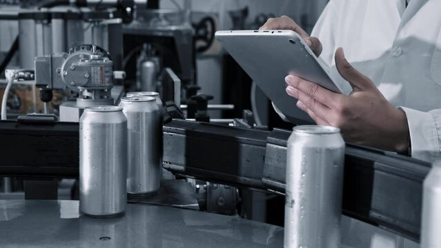Male worker types on a tablet near conveyor with cans at beverage factory production line, close up. High quality 4k footage